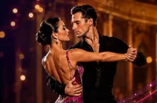 A couple in formal ballroom dance attire dance gracefully against a blurred, warmly lit background.