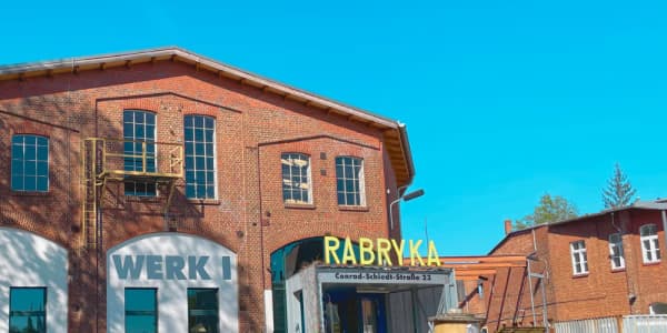 Historic red brick industrial building named Rabryka under a clear blue sky.