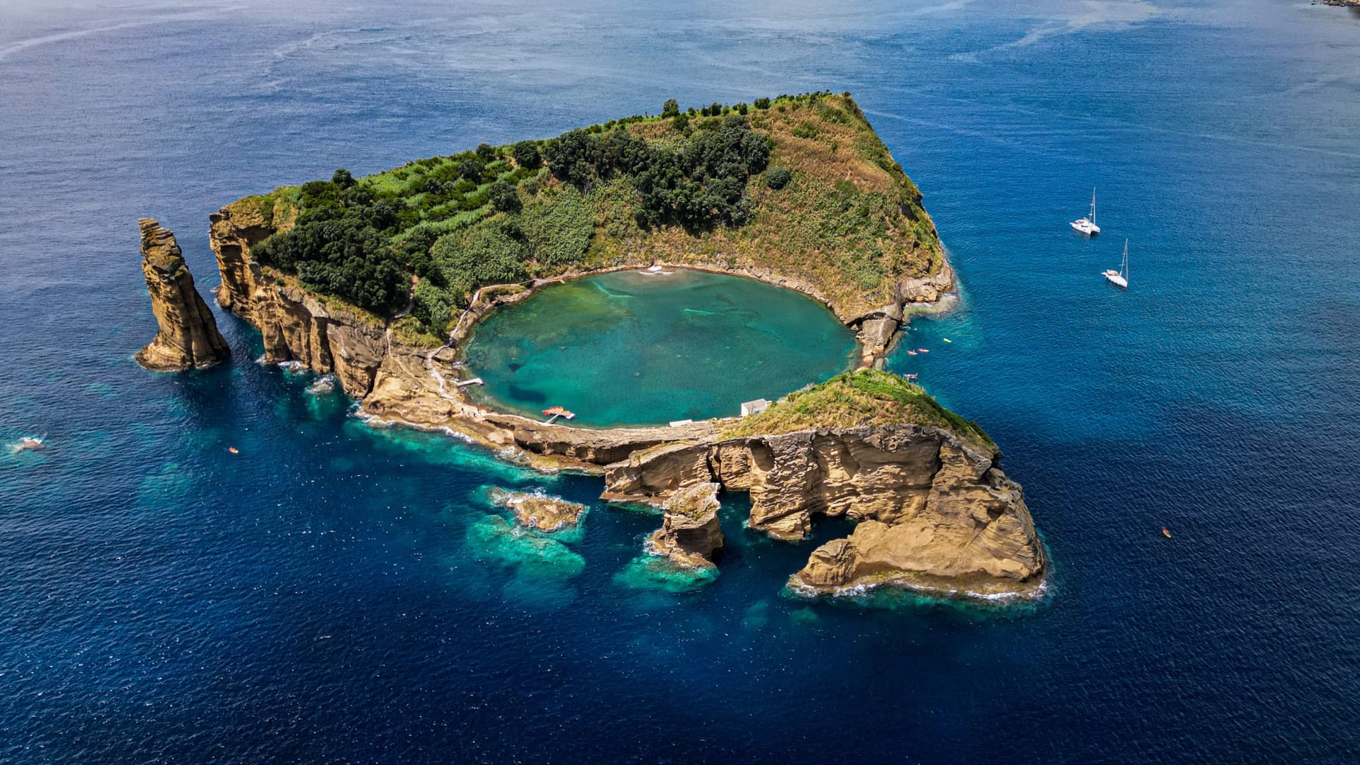 Aerial view of a volcanic islet with a central circular lagoon surrounded by the deep blue ocean.