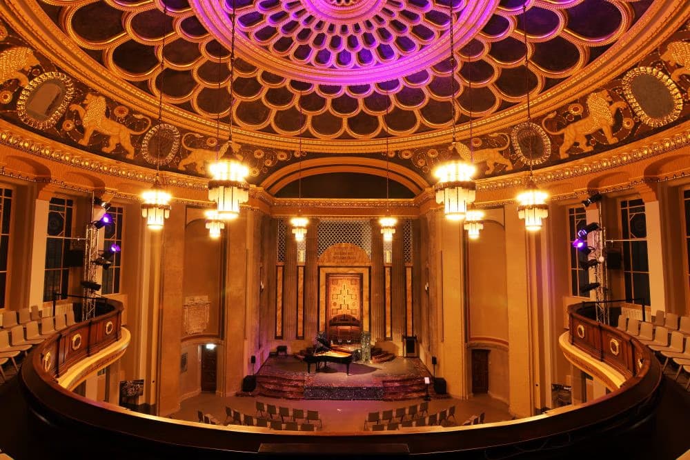 View from the balcony of an ornate, circular concert hall with a stage and seating.