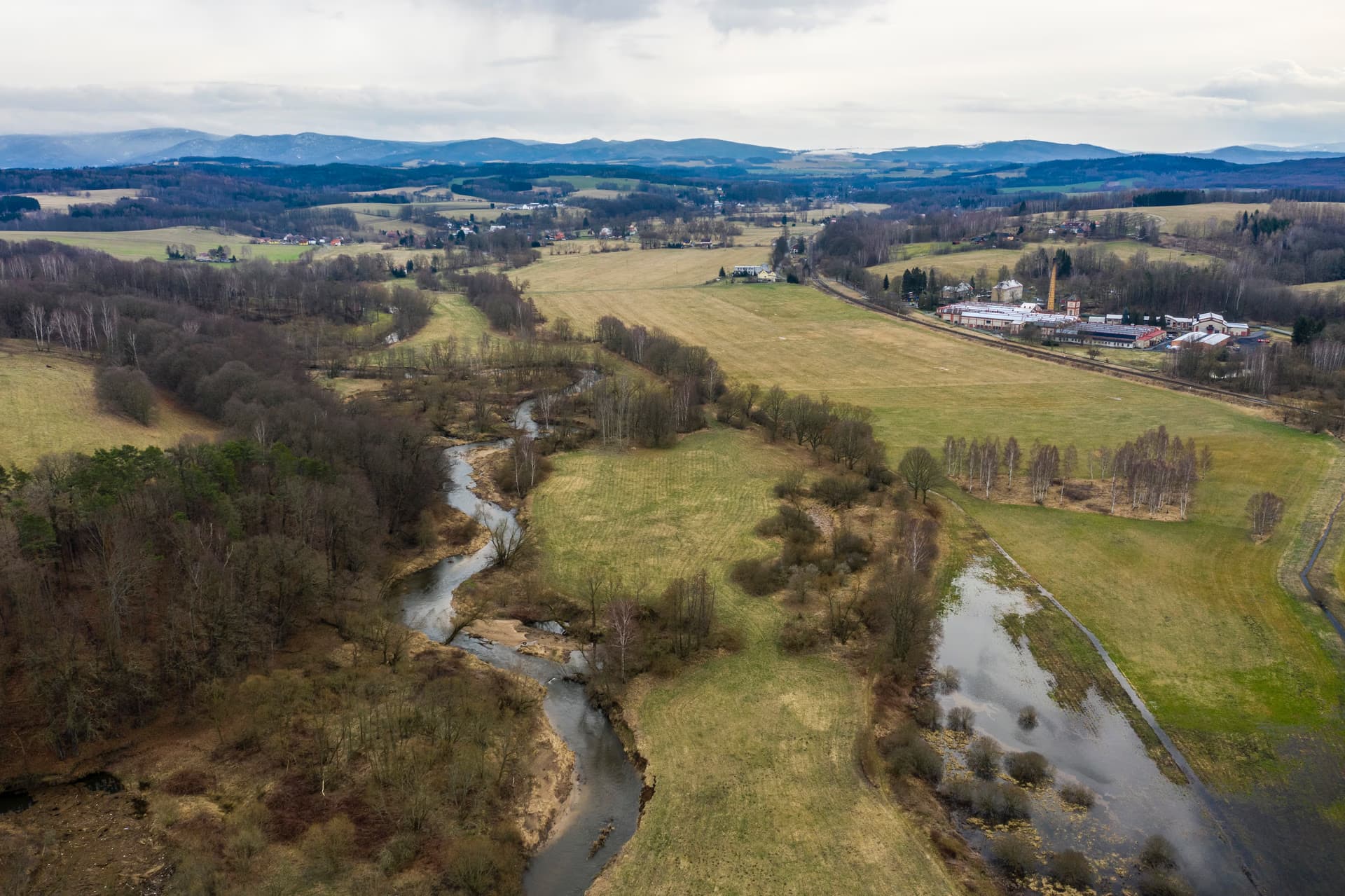 Luftaufnahme eines gewundenen Flusses, der durch grüne Felder und Wälder in einer hügeligen Landschaft fließt.