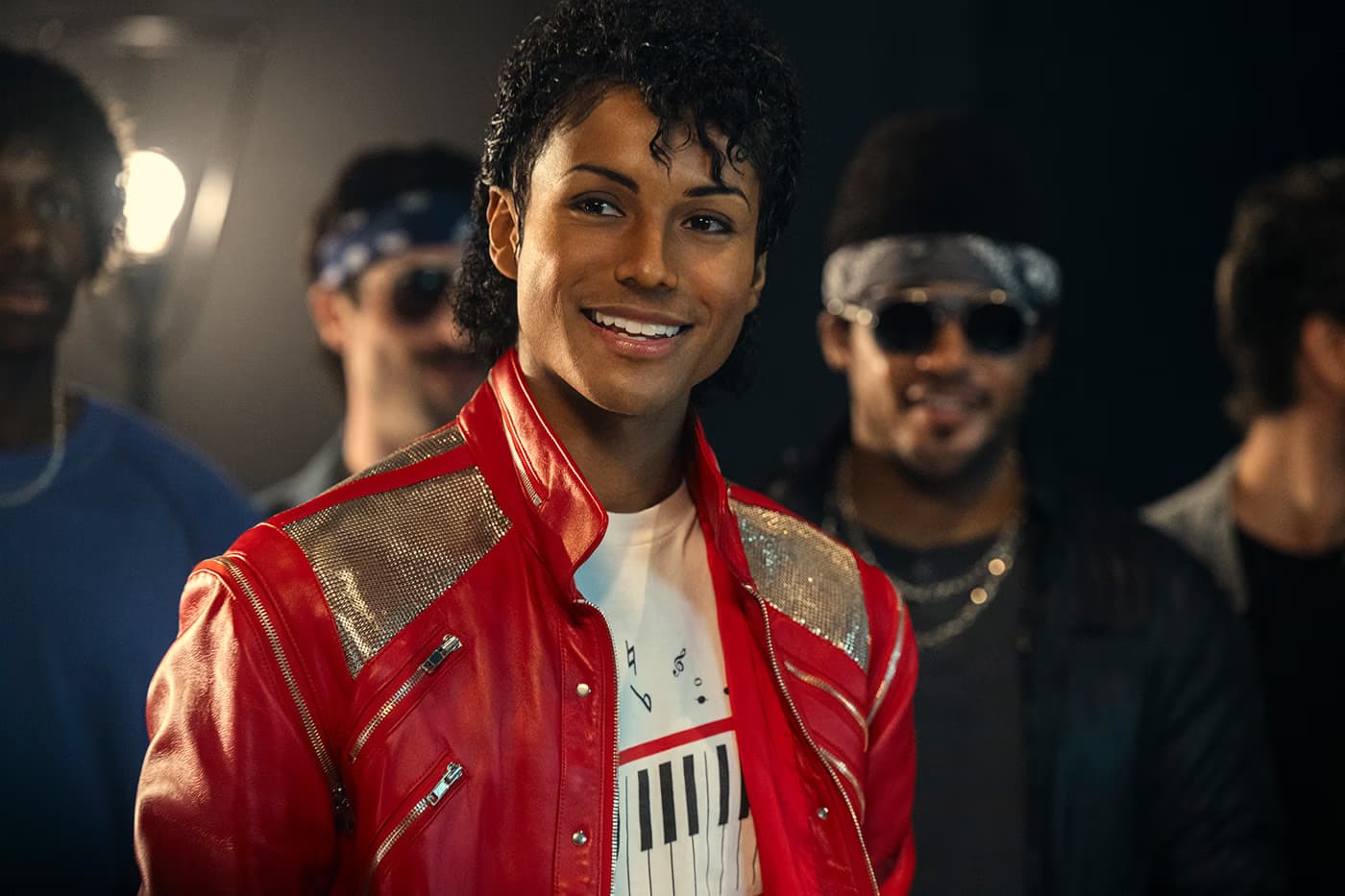 A Michael Jackson impersonator in a red leather jacket stands smiling surrounded by a group of people.