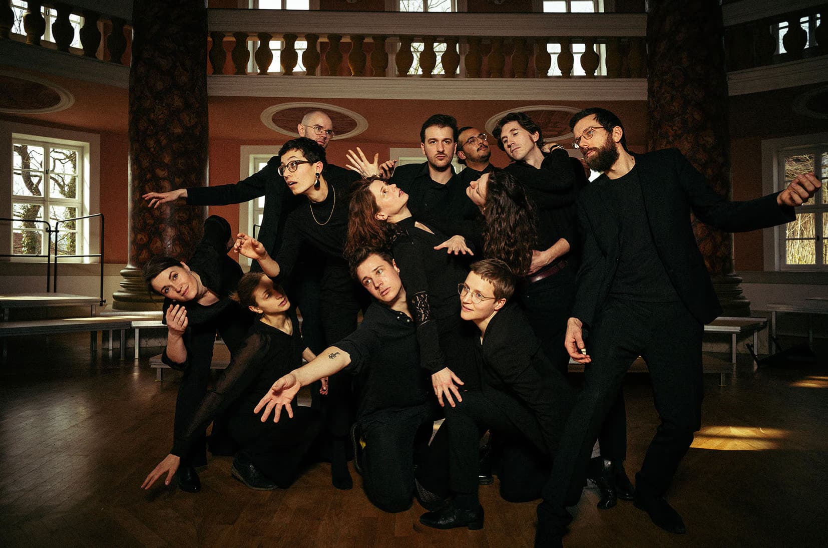 A group of people in black clothing posing artistically inside a large, circular, hall-like room.