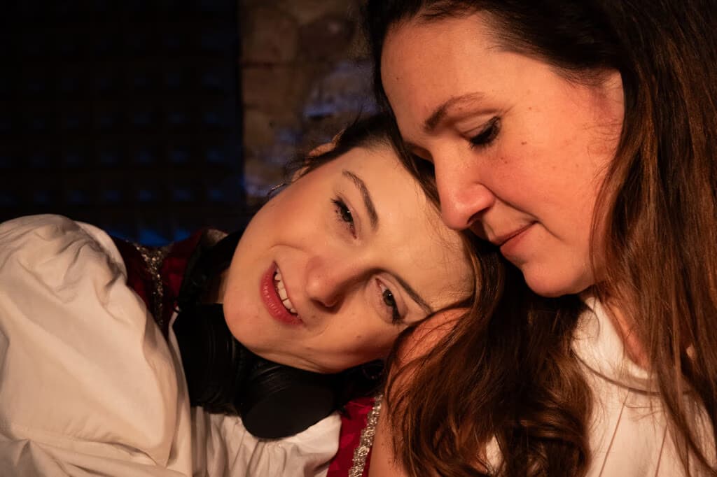Two women with long hair lean their heads together in a close, intimate moment.