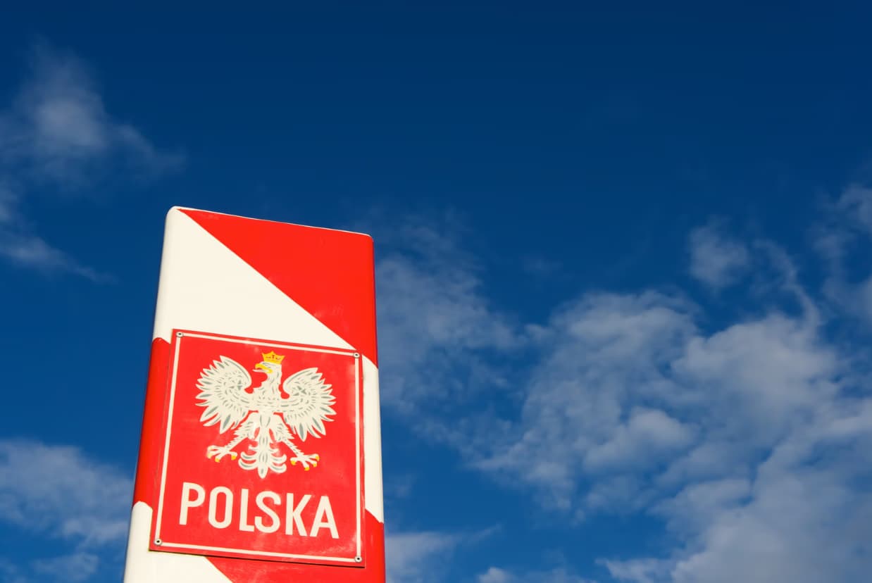 Polish border marker post featuring the national eagle emblem against a bright blue sky.