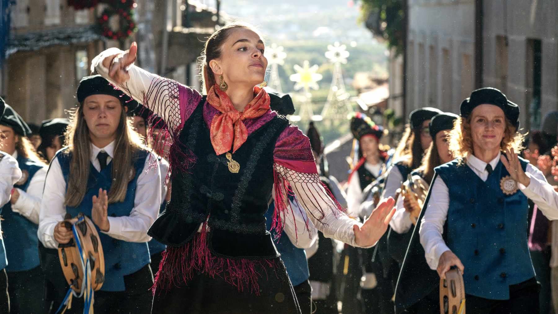 Eine Frau in traditioneller Tracht tanzt im Freien, begleitet von einer Gruppe mit Tamburinen.