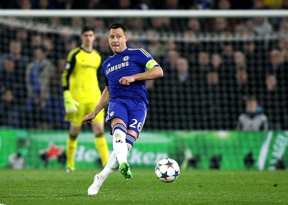 Fotbalista Chelsea v modrém dresu kope do míče během zápasu na hřišti.