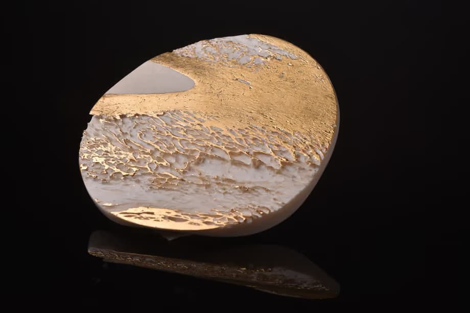 A textured golden ceramic disc rests against a stark black background.