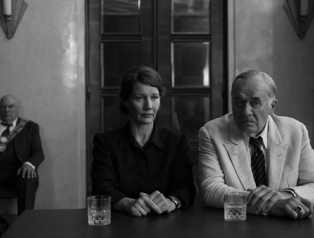 Three people in formal attire sit indoors in this black and white scene.