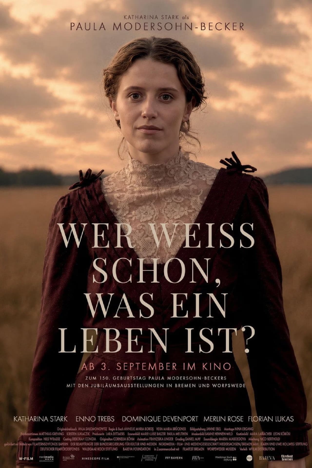 Eine junge Frau in historischer Kleidung steht bei Sonnenuntergang auf einem Feld und blickt zur Kamera.