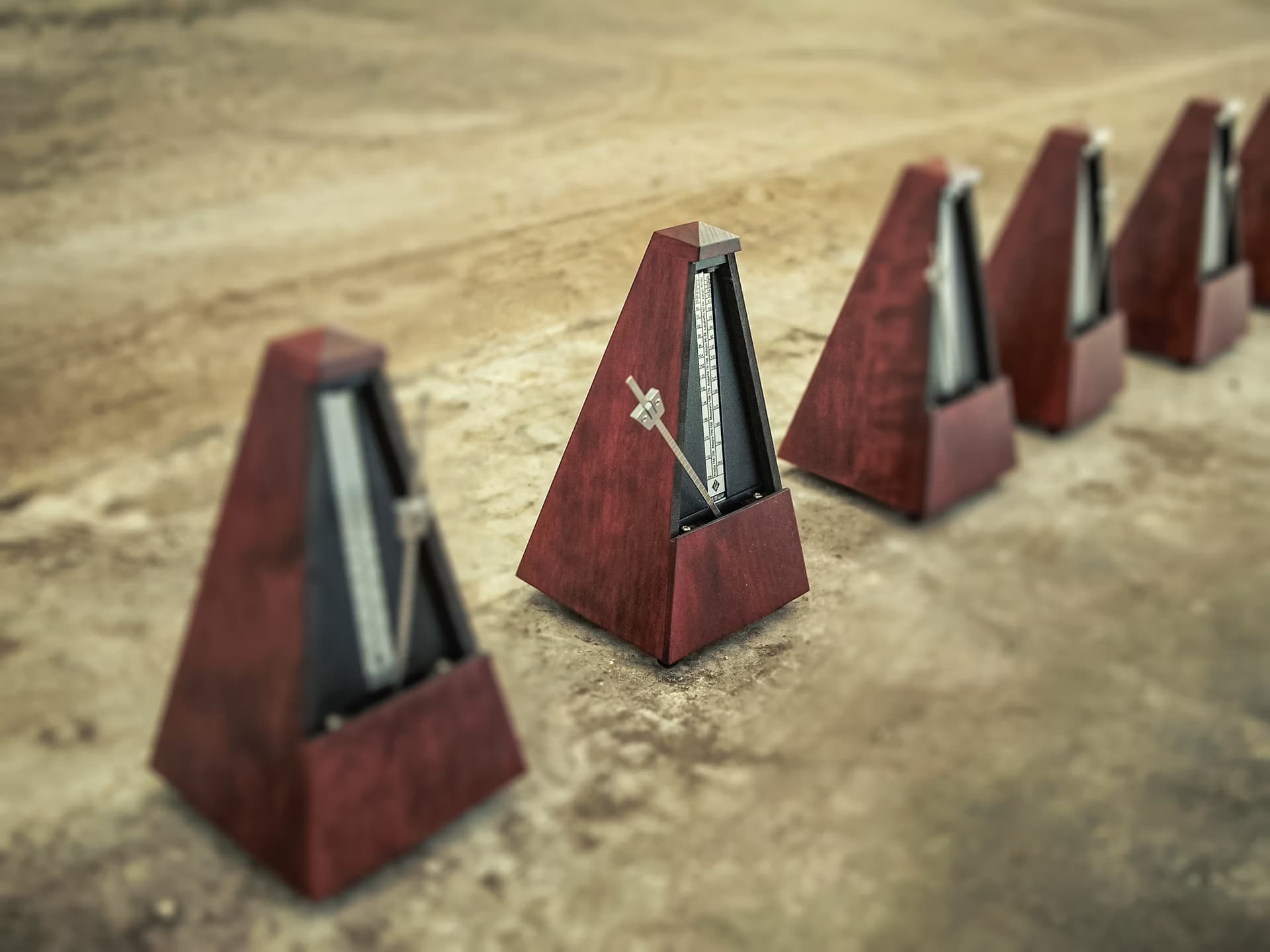 A row of several wooden mechanical metronomes stands on a textured brown surface.