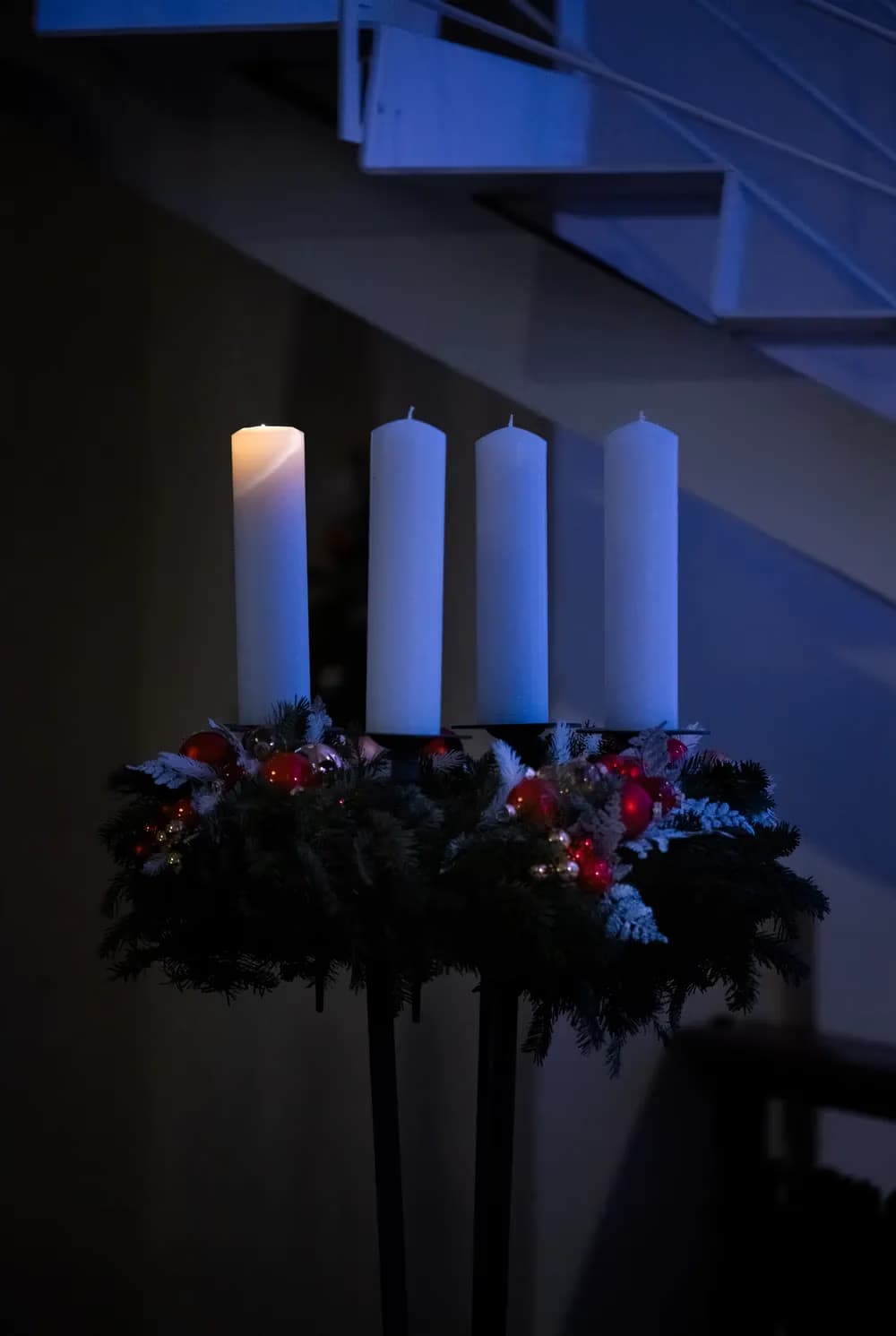 A lit Advent candle stands among three unlit candles on a decorated Christmas wreath.