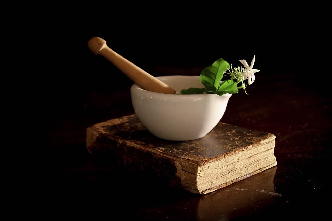 A white mortar and pestle sit on an old, worn book against a dark background.