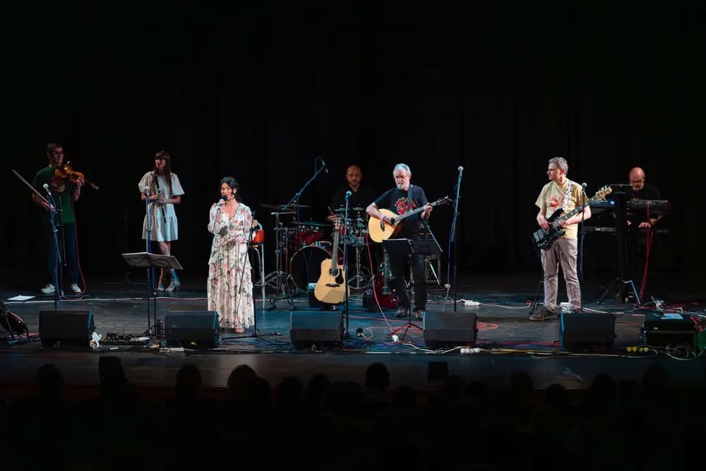 A band with a singer and musicians performs on a dark stage with equipment.