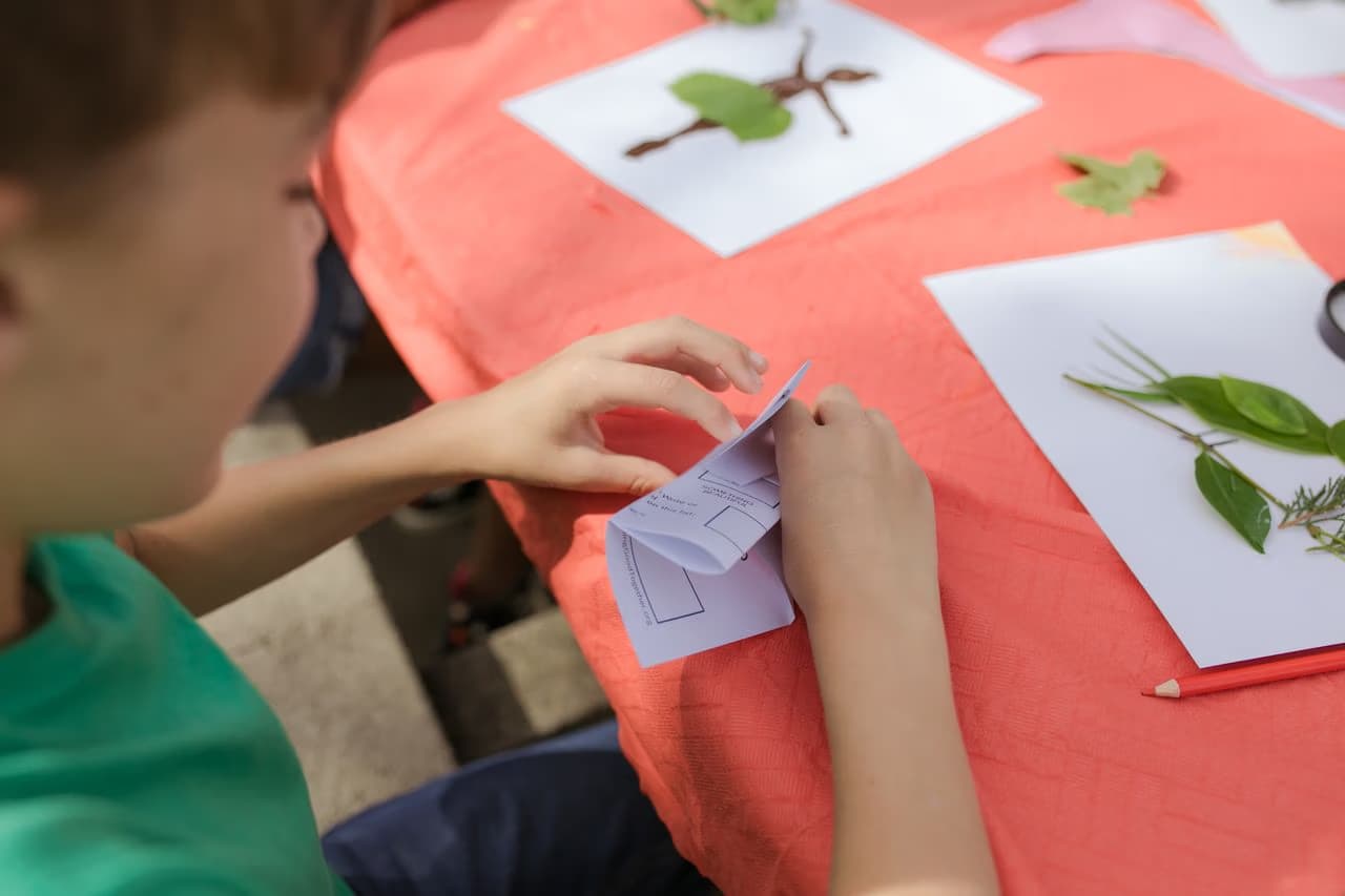 A child in a green shirt folds paper during an outdoor nature-themed craft activity.