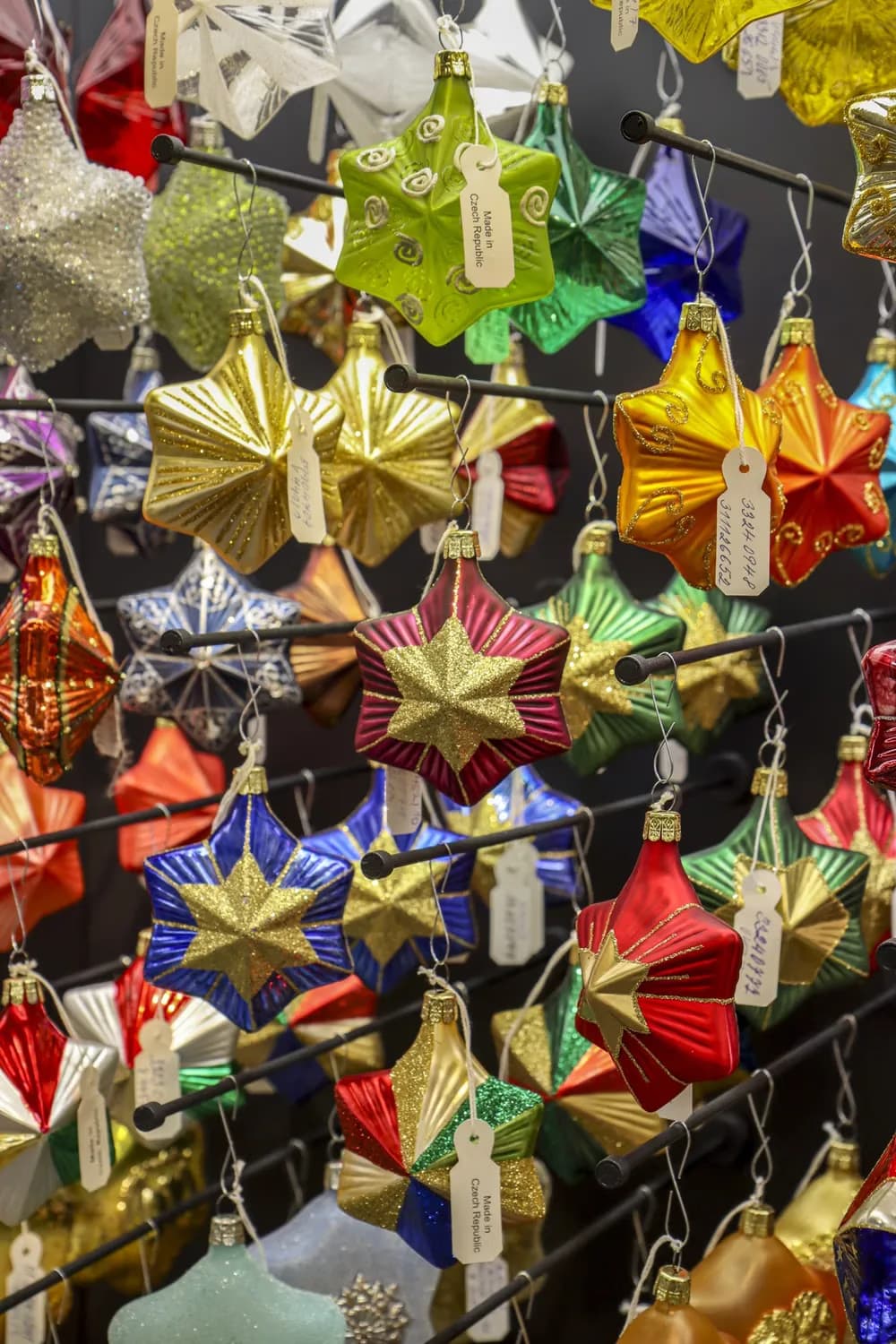 Viele bunte, sternförmige Weihnachtskugeln aus Glas hängen an einem Verkaufsständer.