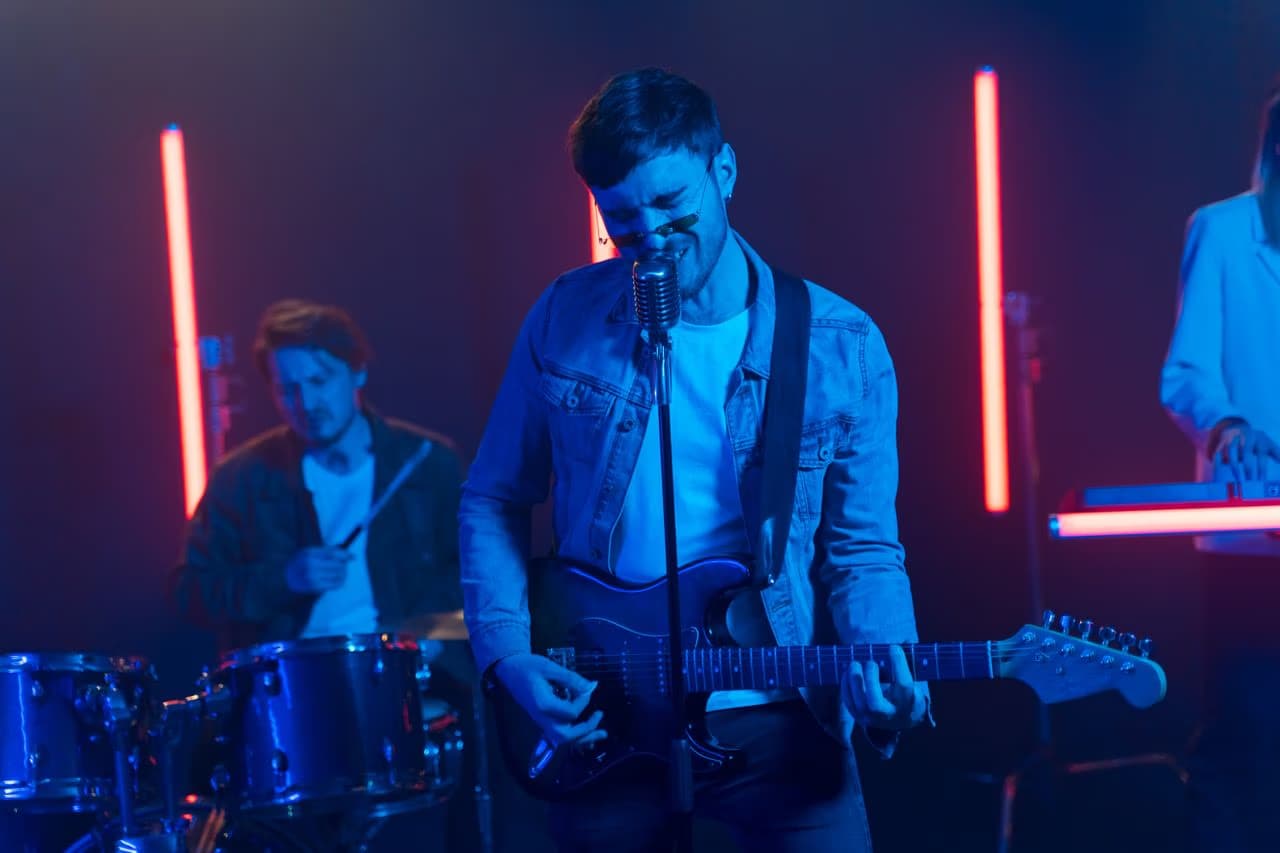 A band performs on a dimly lit stage with blue and red neon lights.