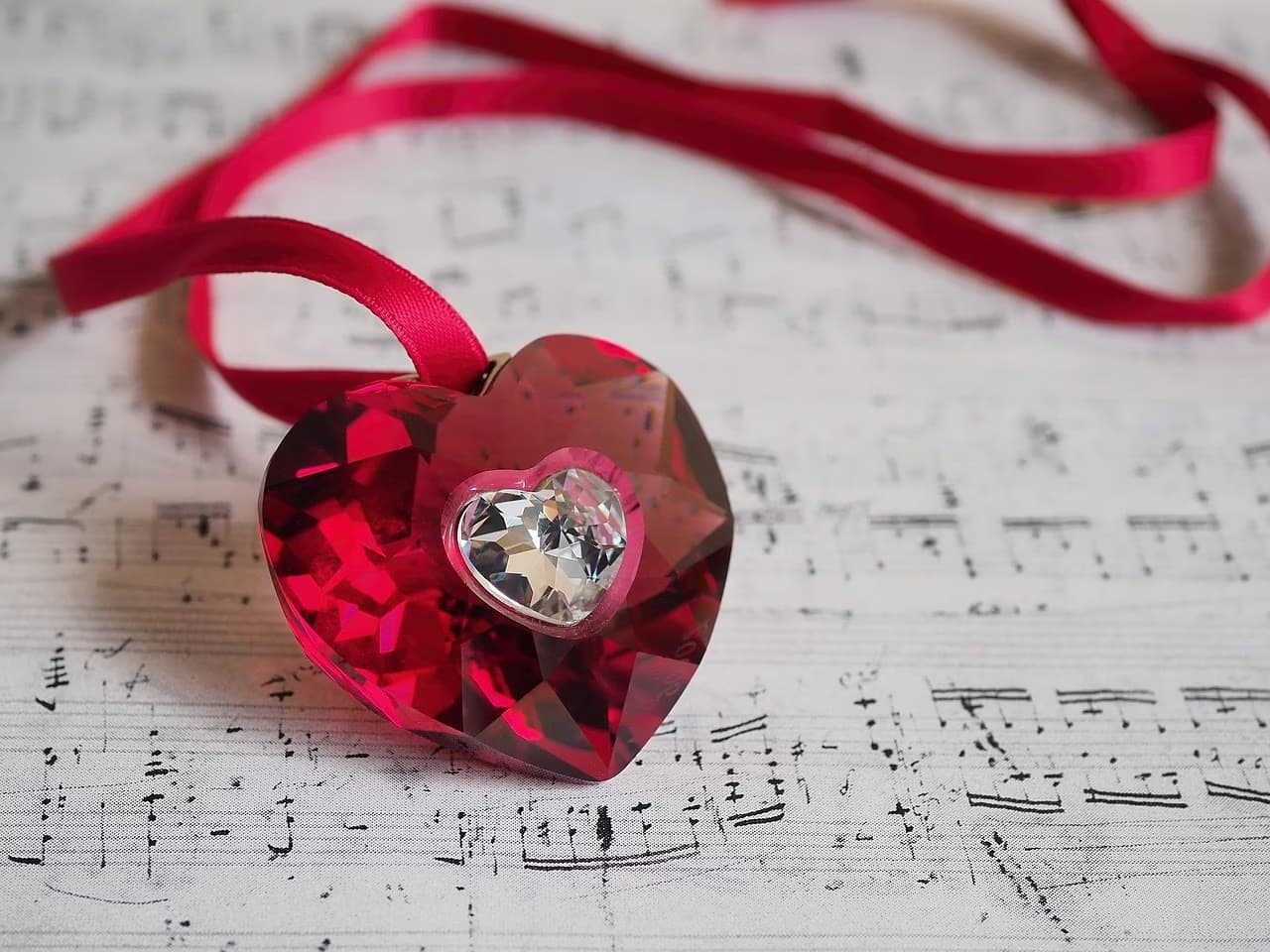 A red crystal heart pendant with a ribbon rests on a sheet of musical notes.