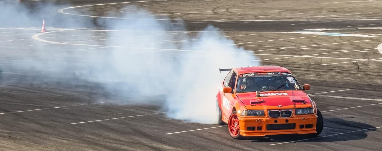 An orange race car drifts around a corner on an asphalt track, leaving a trail of smoke.