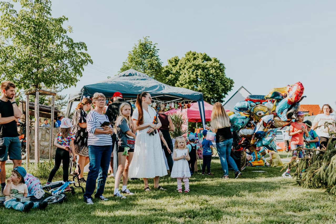People gather on a sunny day at an outdoor festival with tents and balloons.