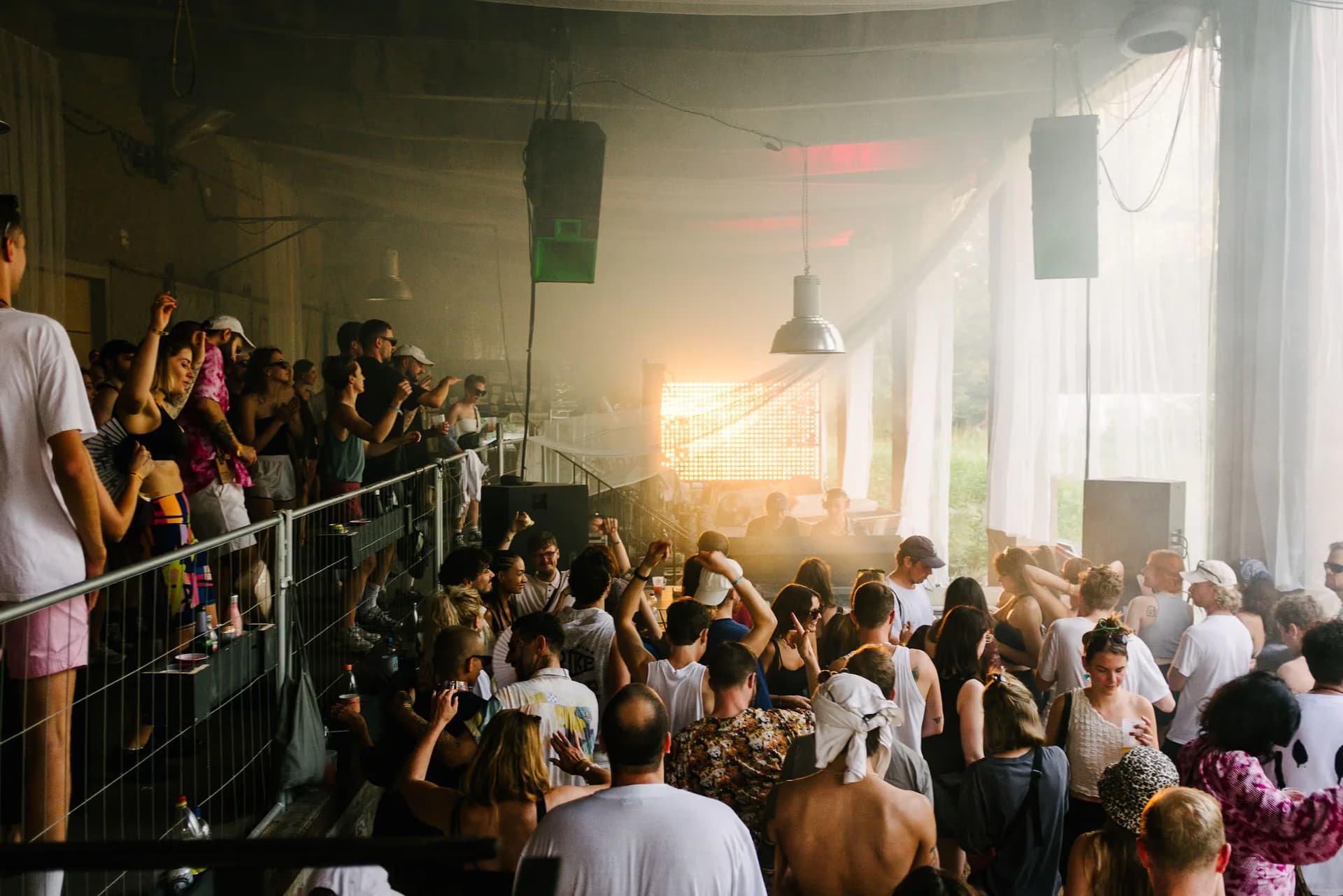 Crowd dancing at a dimly lit indoor music event with stage lights and smoke.