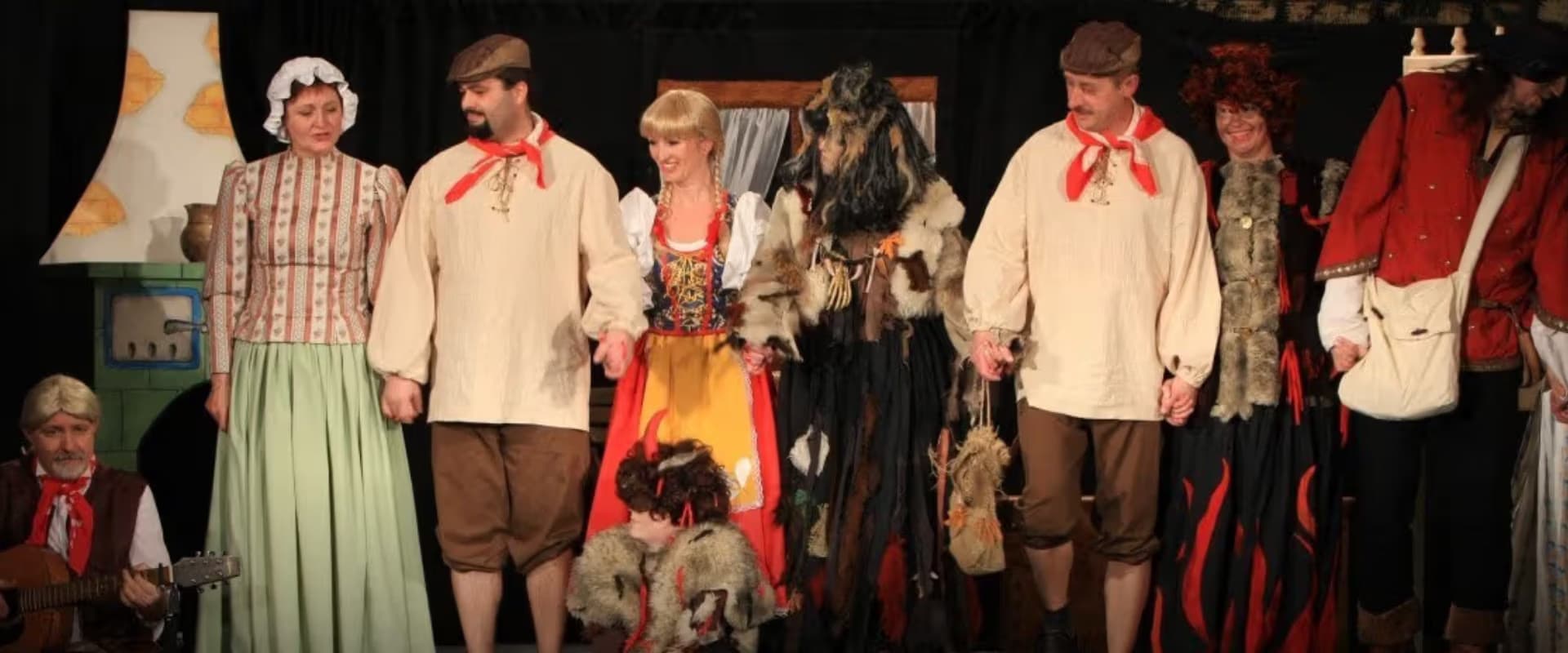 Actors in traditional folk costumes perform on a dark theatrical stage together.