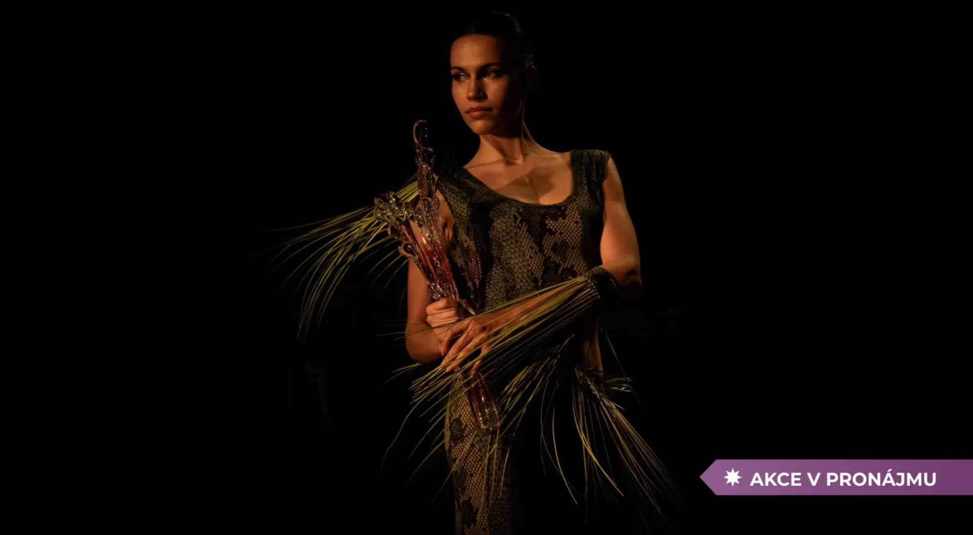 A woman in a costume made of fibrous materials poses against a dark background.