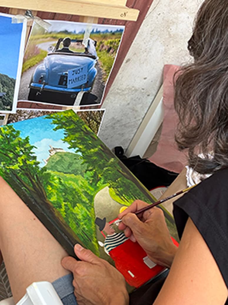 An artist paints a landscape featuring a hill with a castle on a canvas.