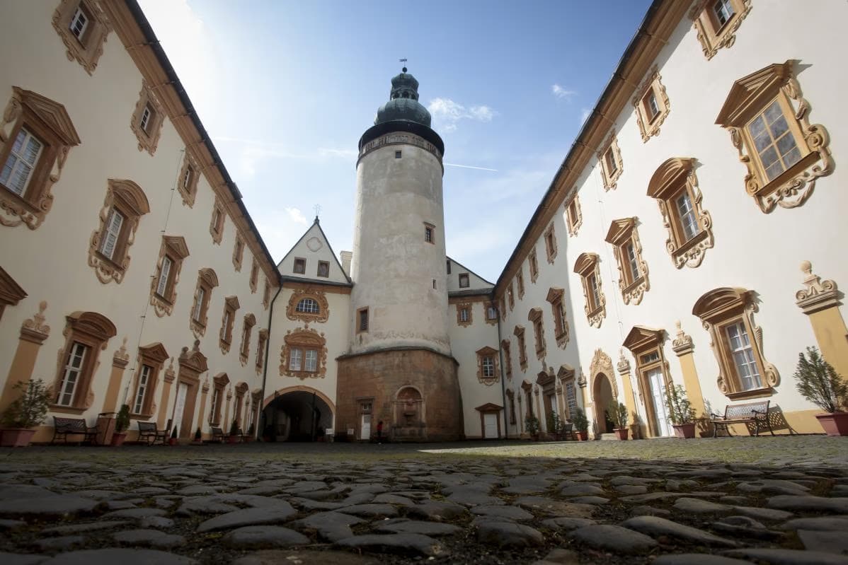 Low-angle view of a stone castle courtyard with a prominent tower and light-colored walls.