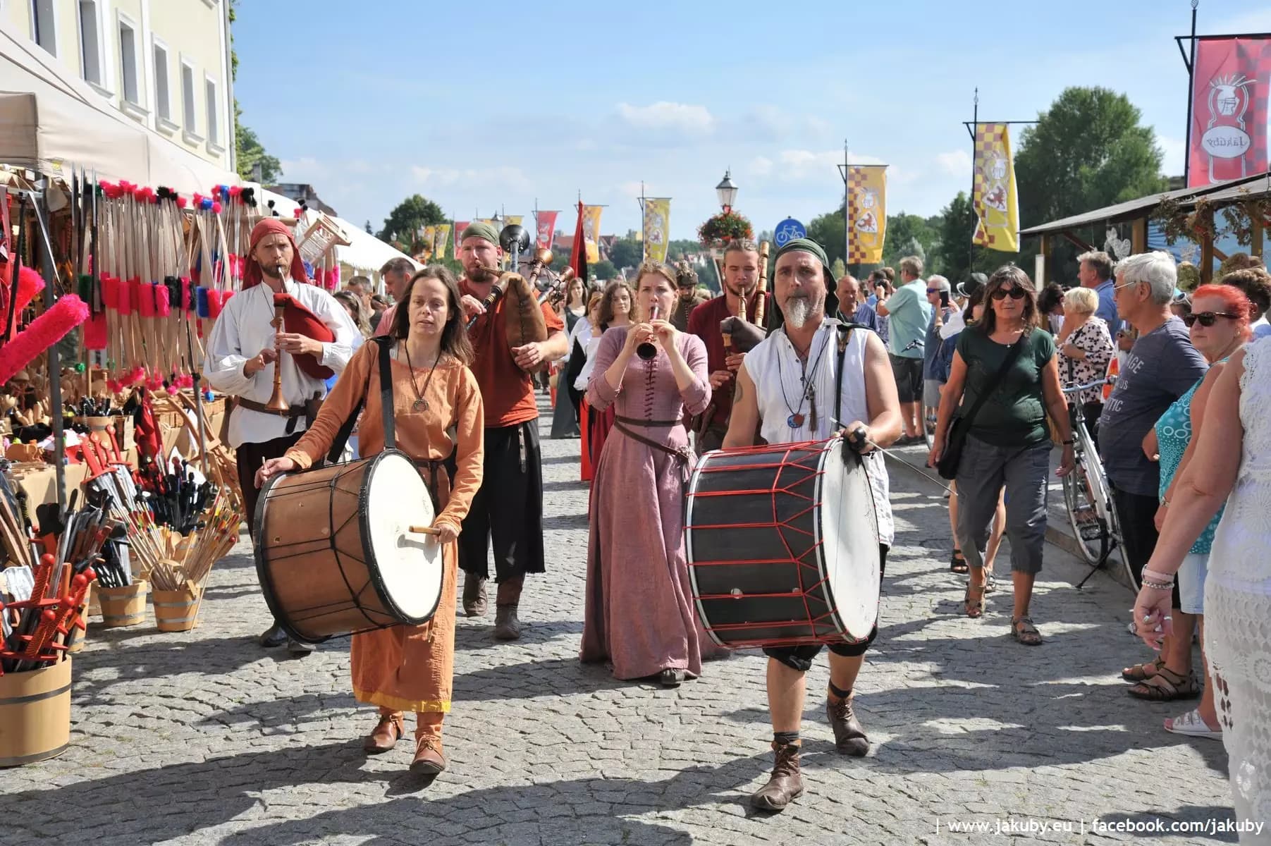 People in historical costumes playing drums and flutes walk down a street at a medieval festival.