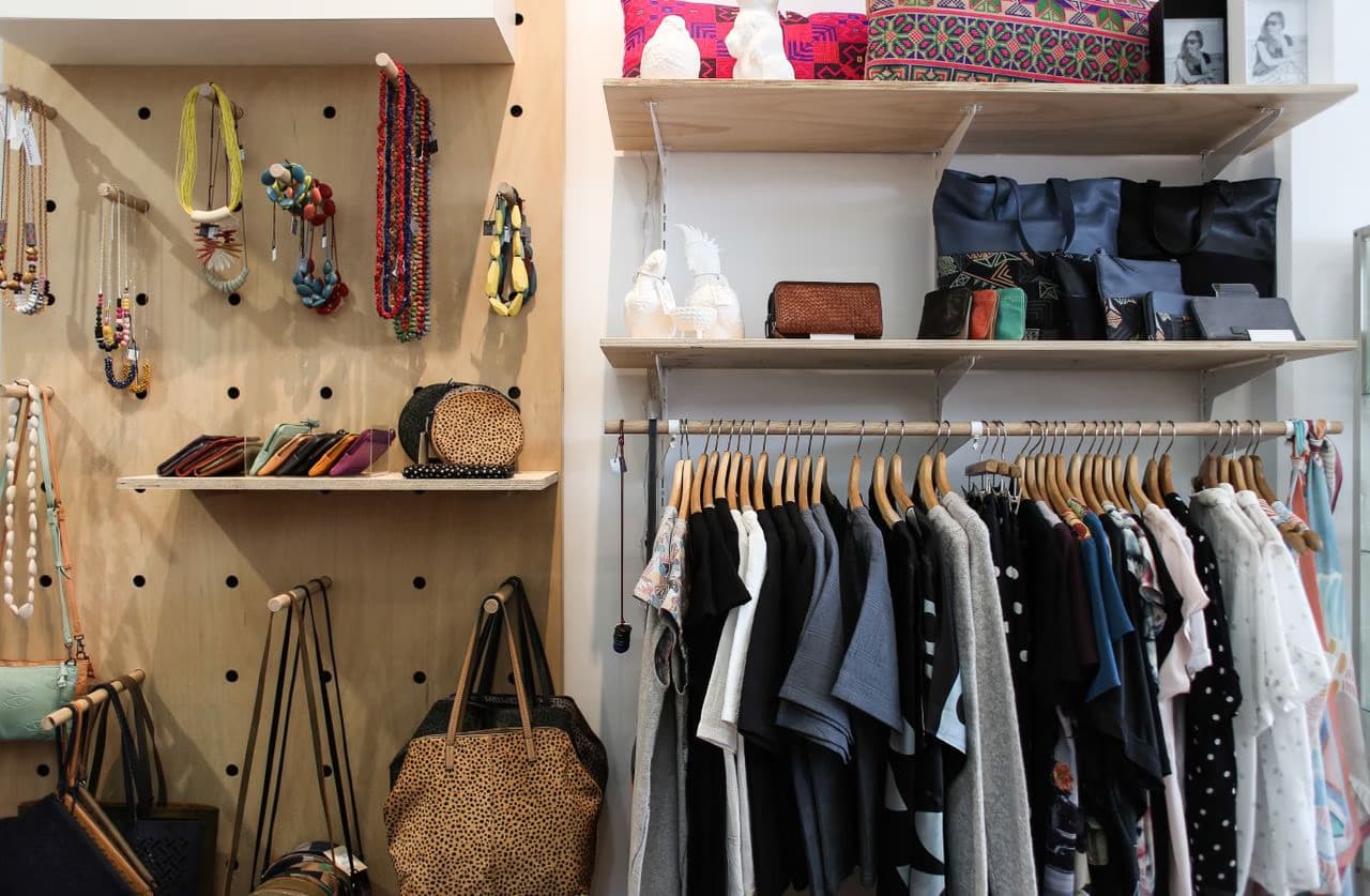 A boutique clothing shop displays clothes on hangers and accessories on shelves and pegboards.