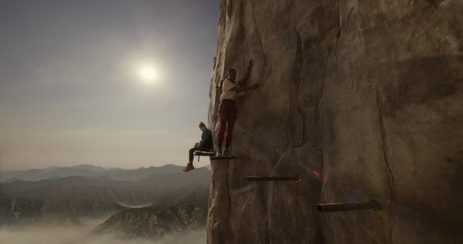 Two people rest on wooden platforms attached to a high rock face overlooking a misty valley.