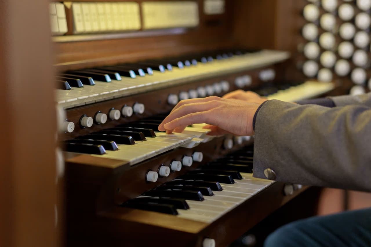 A close-up of a musician's hand playing the manuals of a wooden pipe organ.