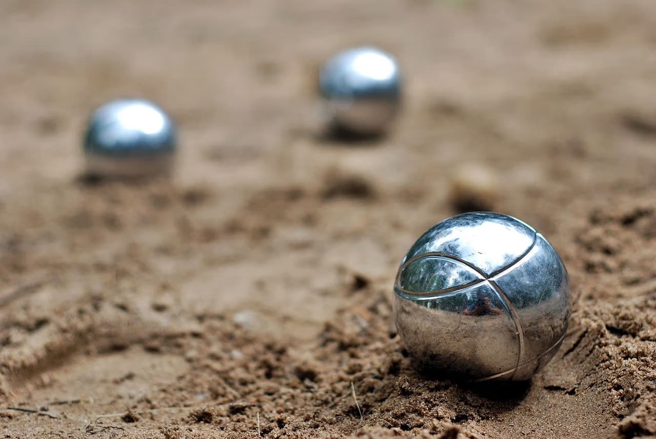 Three metallic petanque boules resting on a sandy court surface.