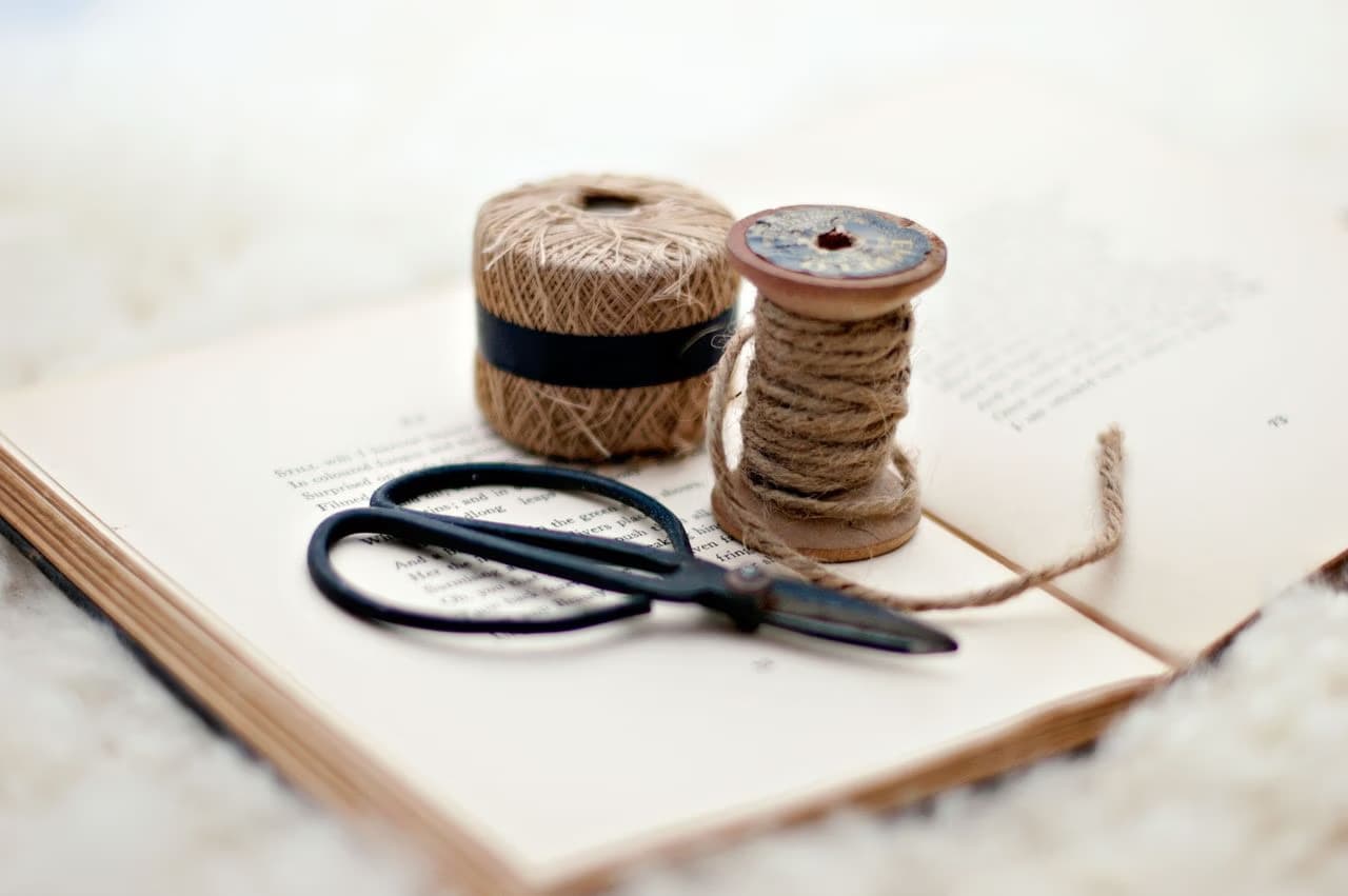 A spool of twine, a ball of string, and scissors rest on an open antique book.
