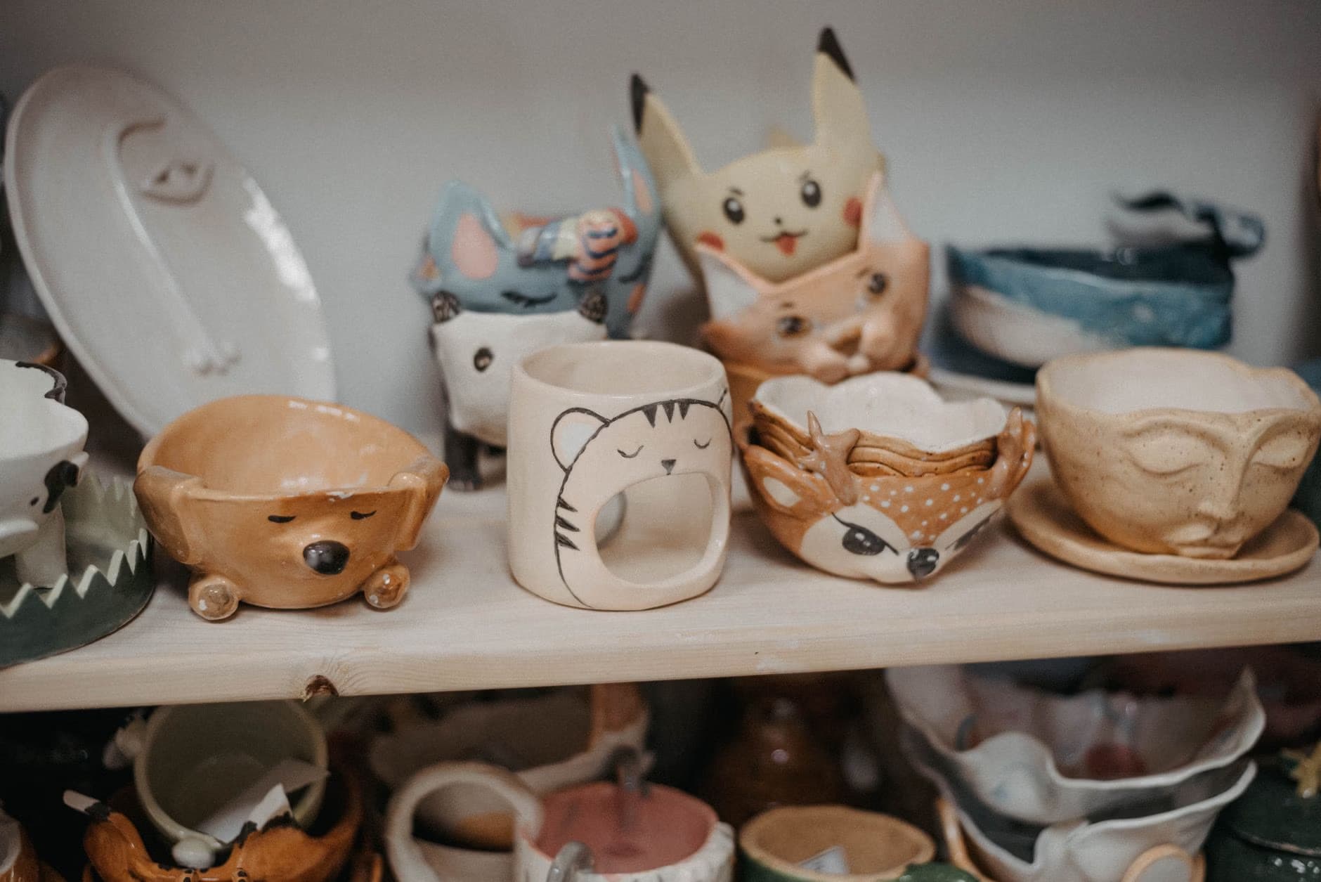 Handmade ceramic bowls and mugs with animal faces sit on wooden shelves.