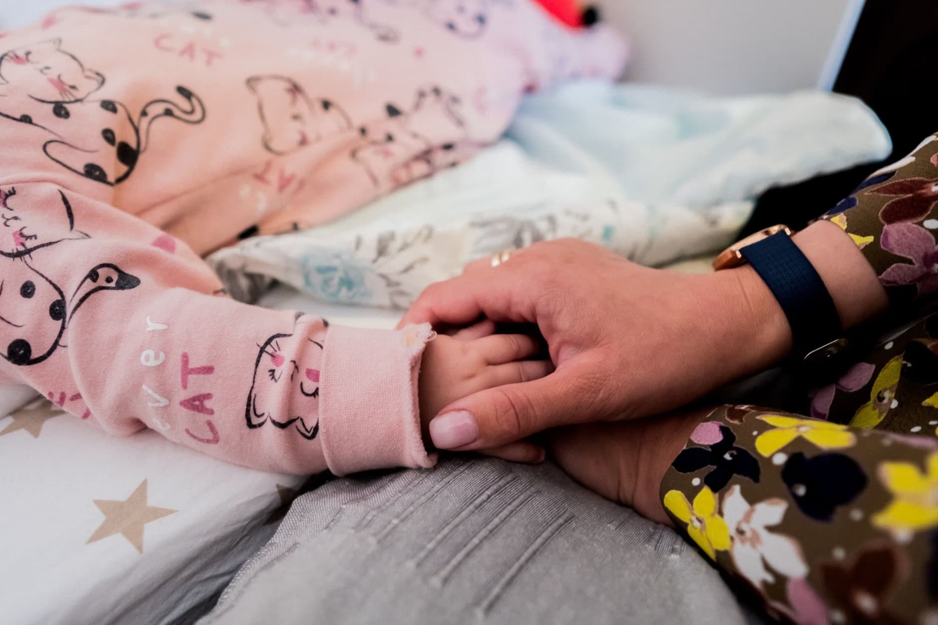 A close-up shot of an adult holding the small hand of a child wearing pink cat-print pajamas.