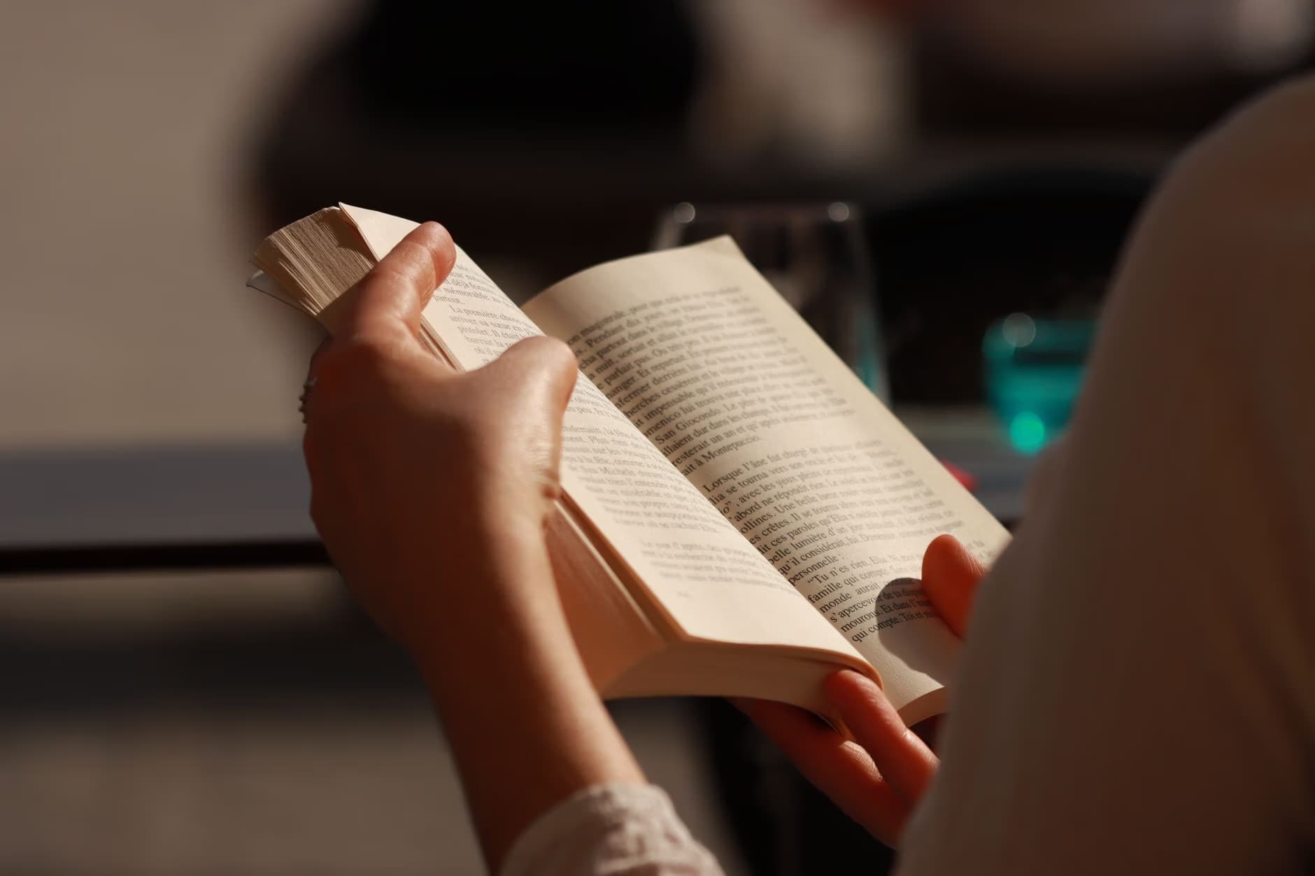 Close-up of a person holding an open book and reading in a dim setting.