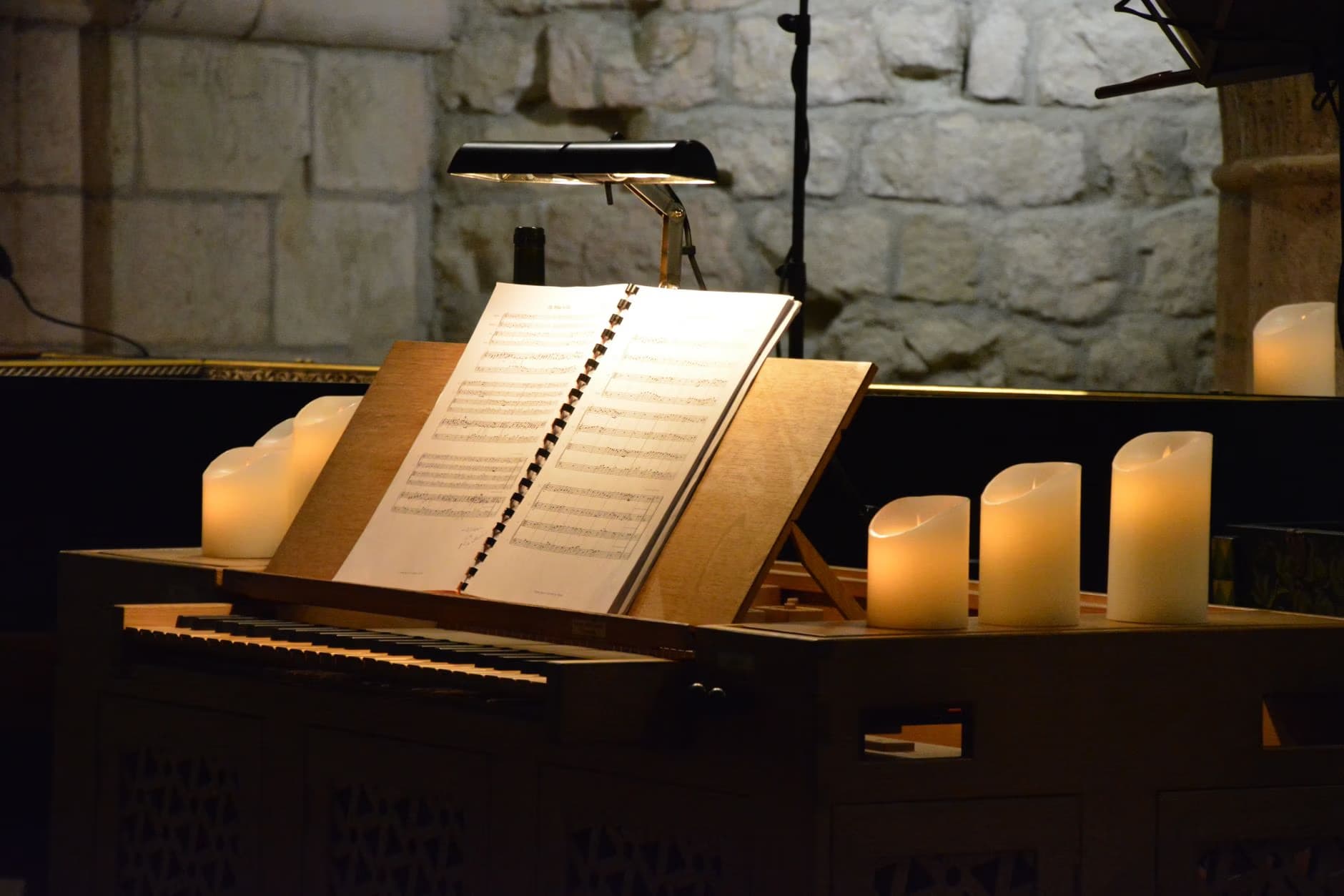 Sheet music on a stand lit by a lamp and candles against a stone wall.
