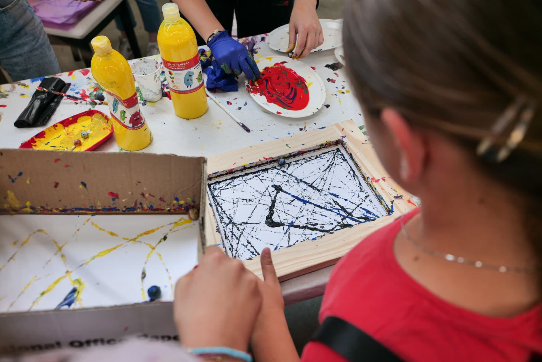 Children engage in an art workshop with paints, brushes, and creative materials on a table.