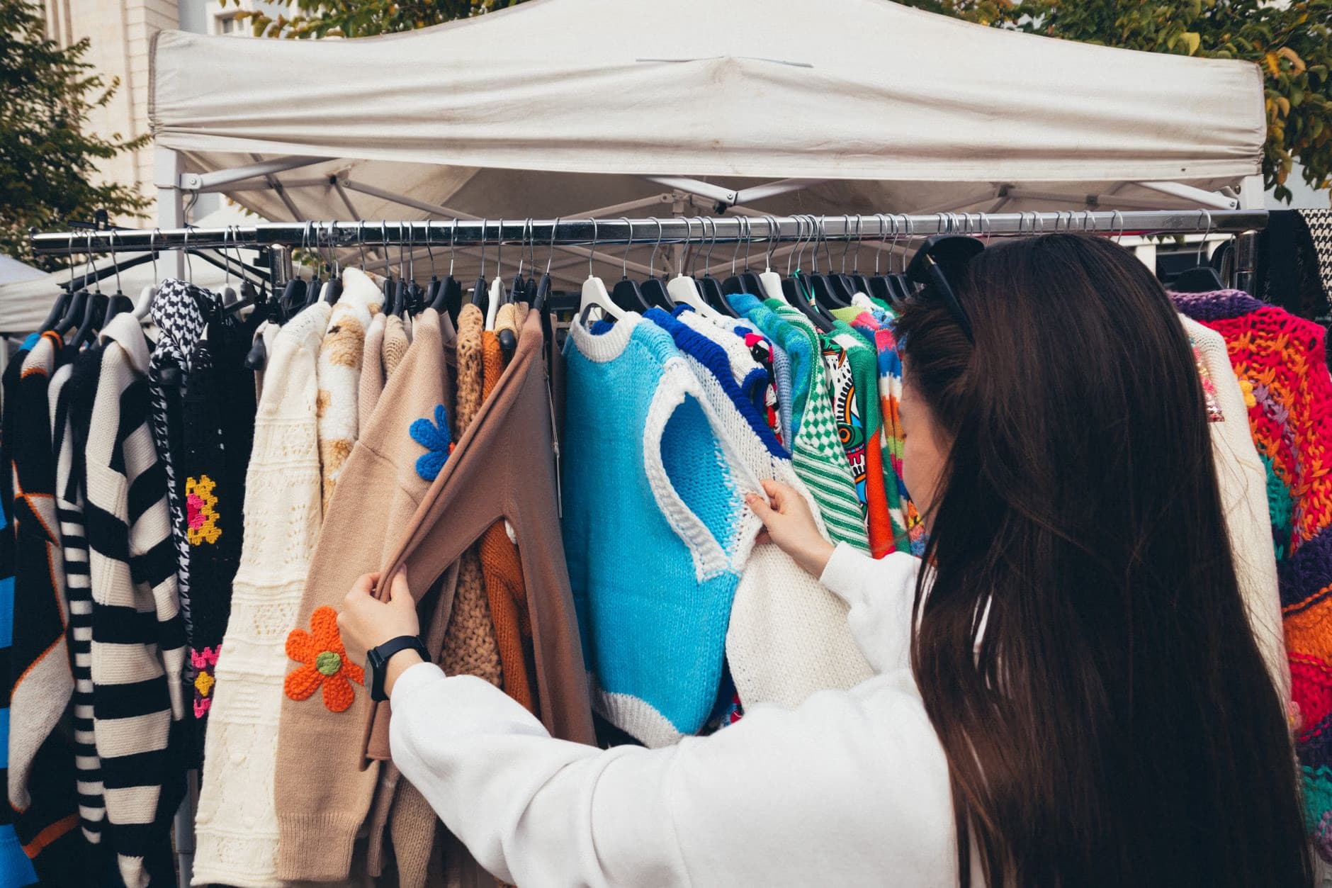 Eine Frau betrachtet bunte Strickpullover auf einer Kleiderstange auf einem Außenmarkt.