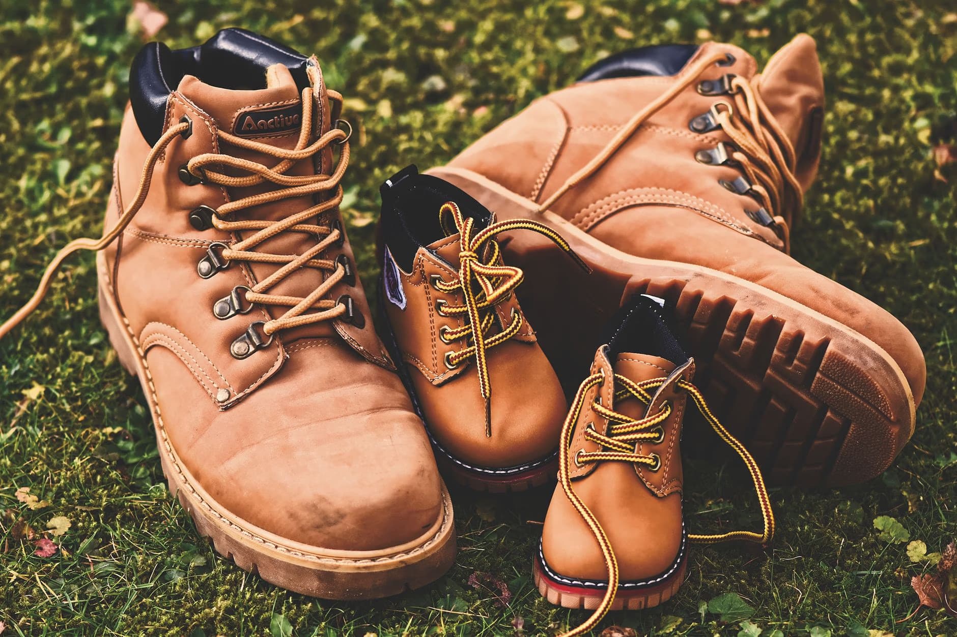 A collection of brown leather boots in varying sizes sits together on green grass.