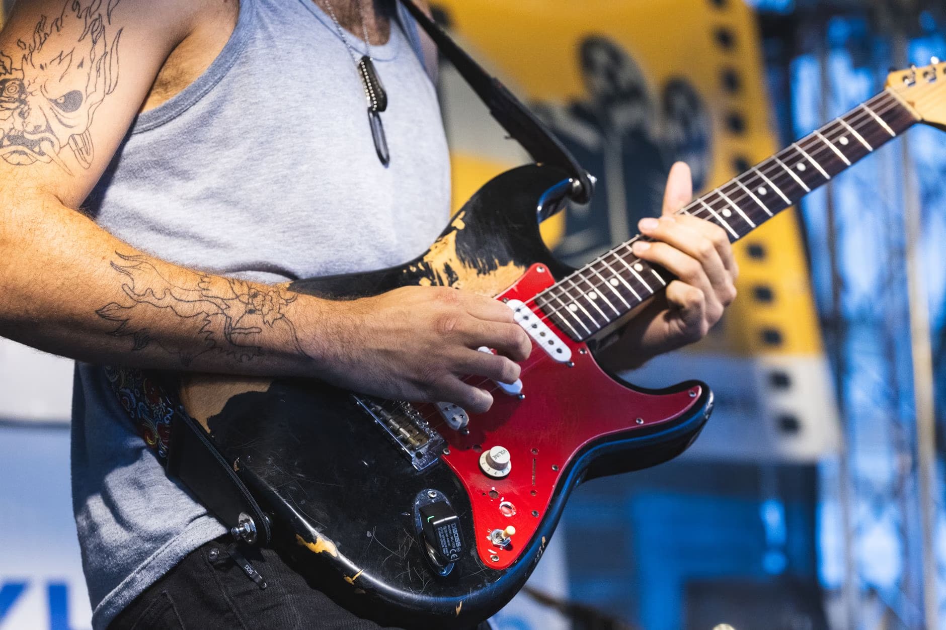 Close-up of a tattooed musician playing an electric guitar on stage at a concert.