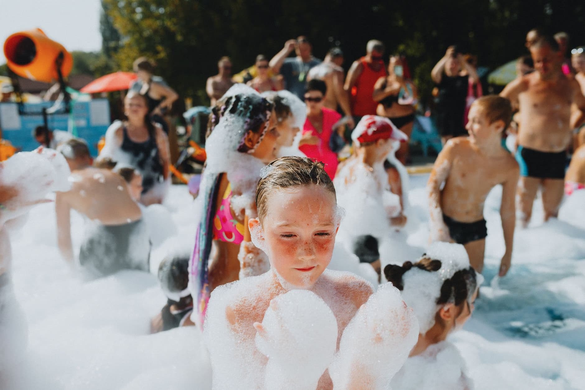 Children play covered in soap bubbles during an outdoor summer foam party event.