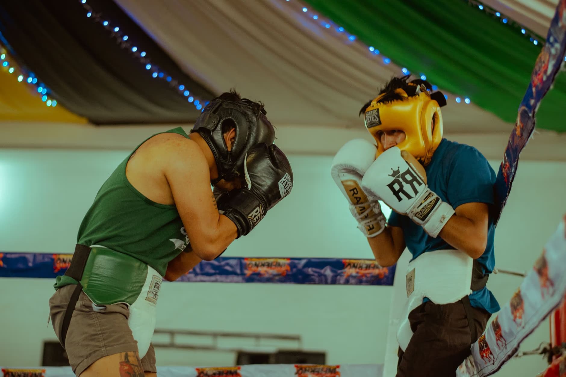 Two boxers wearing headgear and gloves spar together inside a boxing ring.