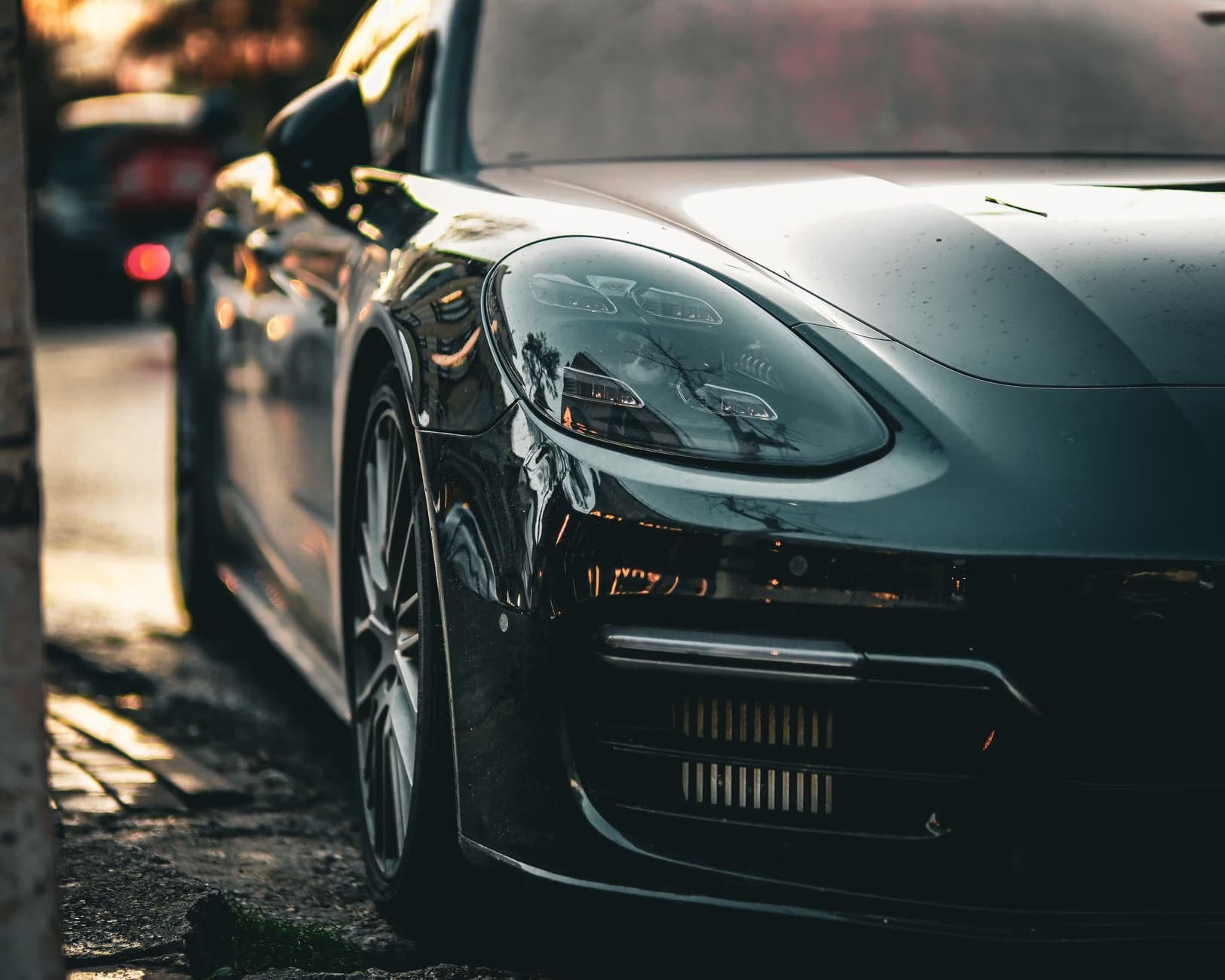 Close up of a dark grey sports car parked on a roadside during sunset.