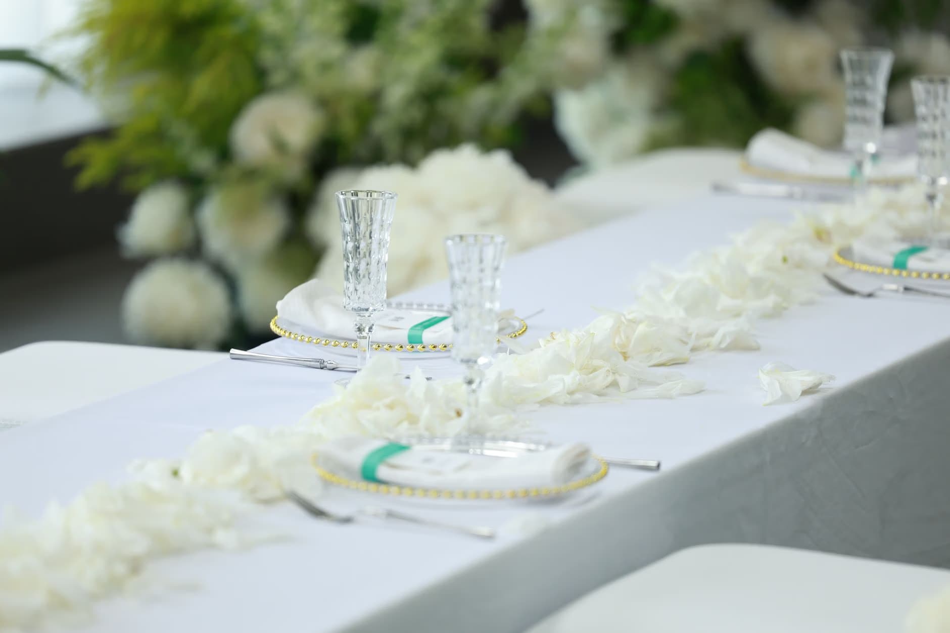A long banquet table is decorated with white flowers, elegant glassware, and neatly folded napkins.
