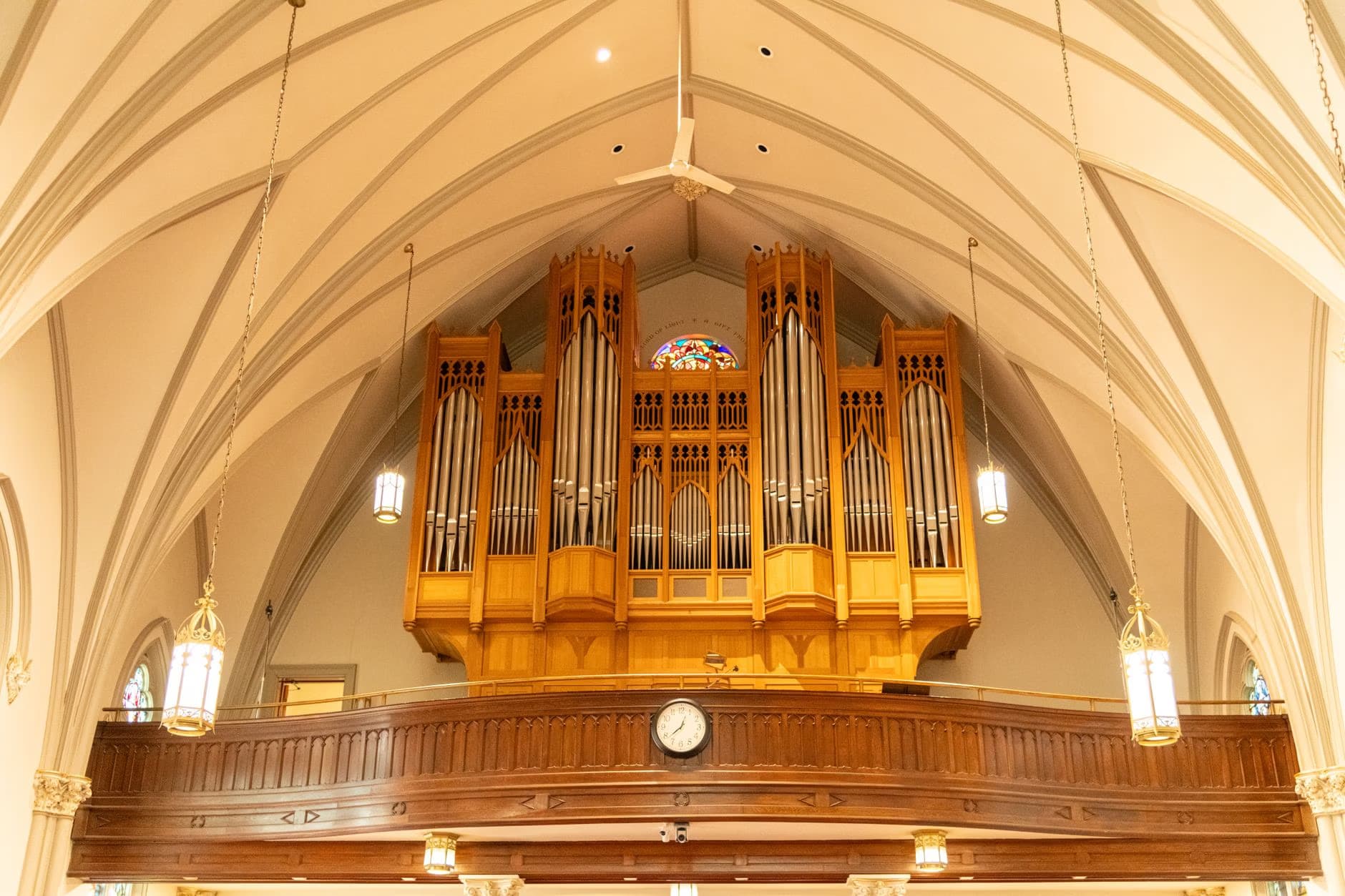 A large pipe organ sits on a wooden balcony beneath the vaulted ceiling of a church interior.
