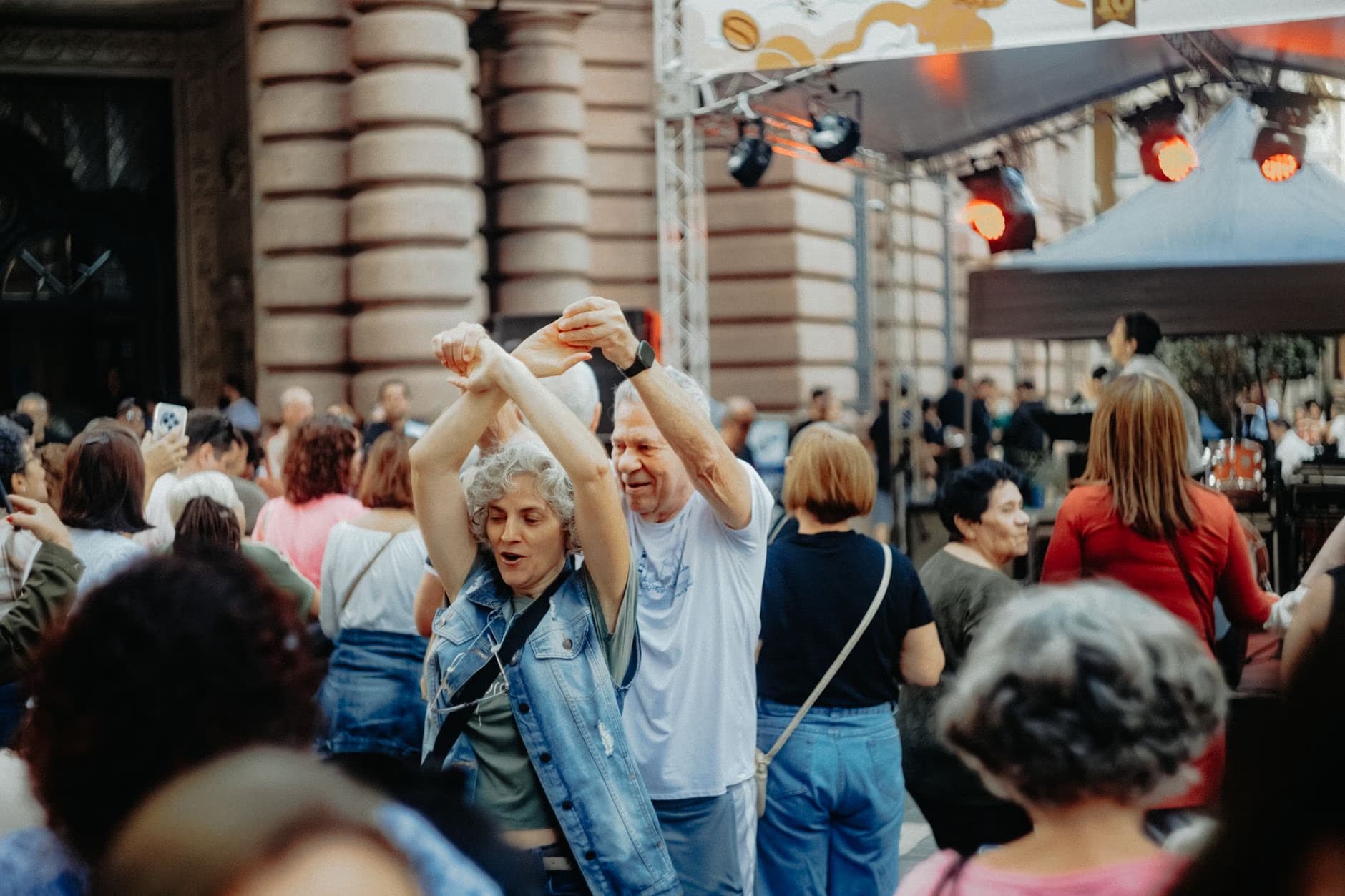 Lidé tančí venku na živém městském festivalu v ulicích poblíž historické budovy.