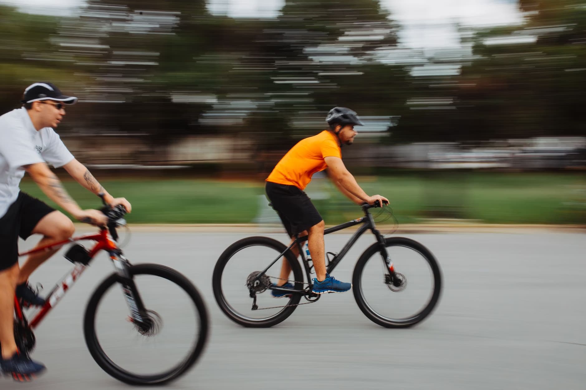 Two cyclists wearing helmets and athletic clothes ride side by side on a paved path.